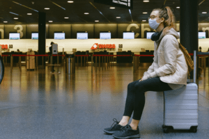 passageira de máscara sentada sobre a mala