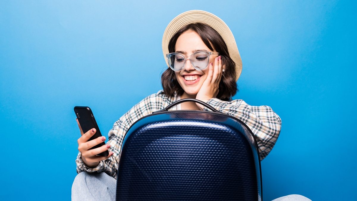 mulher com celular e mala de viagem