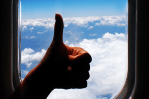 Pessoa fazendo sinal de positivo na janela do avião