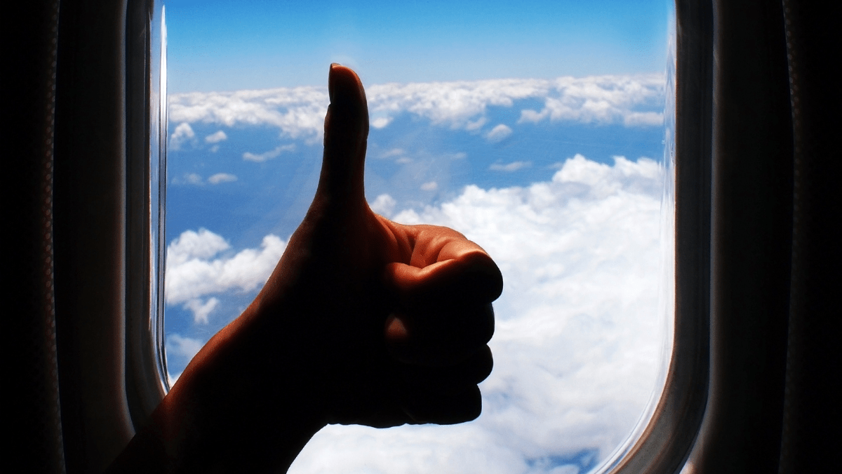 Pessoa fazendo sinal de positivo na janela do avião