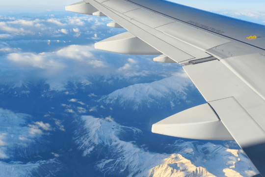 Avião comercial em voo sobre montanhas com paisagem de inverno