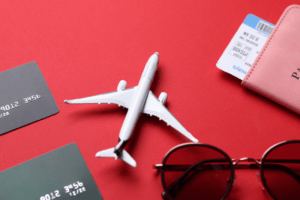 Avião em miniatura ao lado de cartões de crédito e passaporte sobre fundo vermelho.