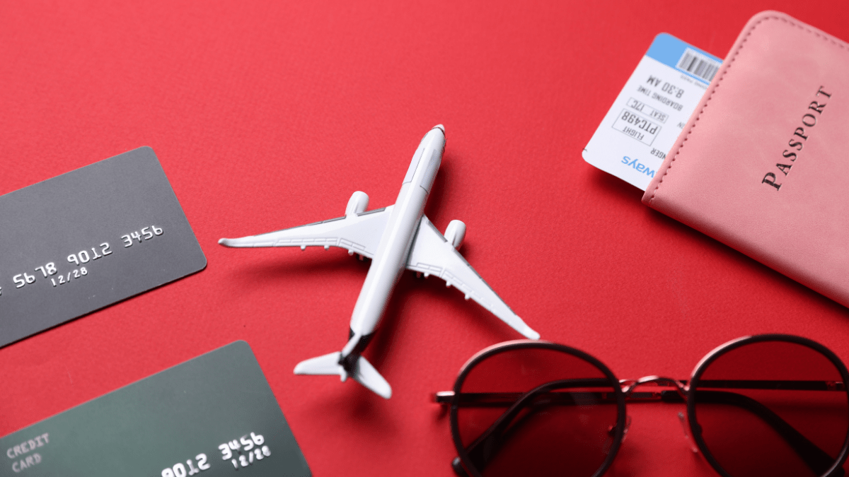 Avião em miniatura ao lado de cartões de crédito e passaporte sobre fundo vermelho.
