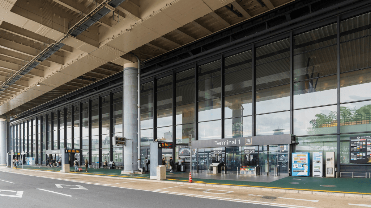 Fachada externa do Terminal 1 de um aeroporto, com área de embarque e desembarque, fachada de vidro e passageiros circulando na entrada