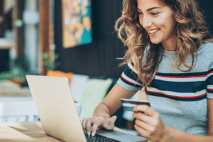 Mulher usando notebook e segurando cartão de crédito em ambiente interno