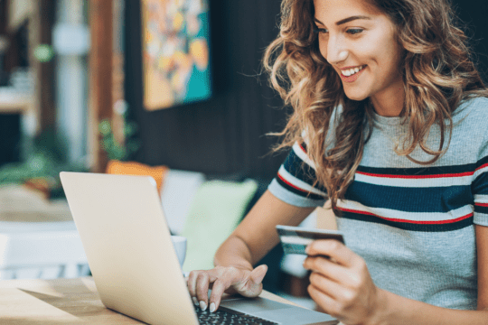 Mulher usando notebook e segurando cartão de crédito em ambiente interno