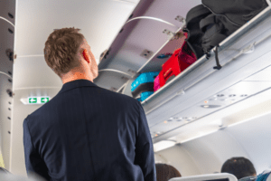 Passageiro em pé na cabine de um avião com malas de mão no compartimento superior