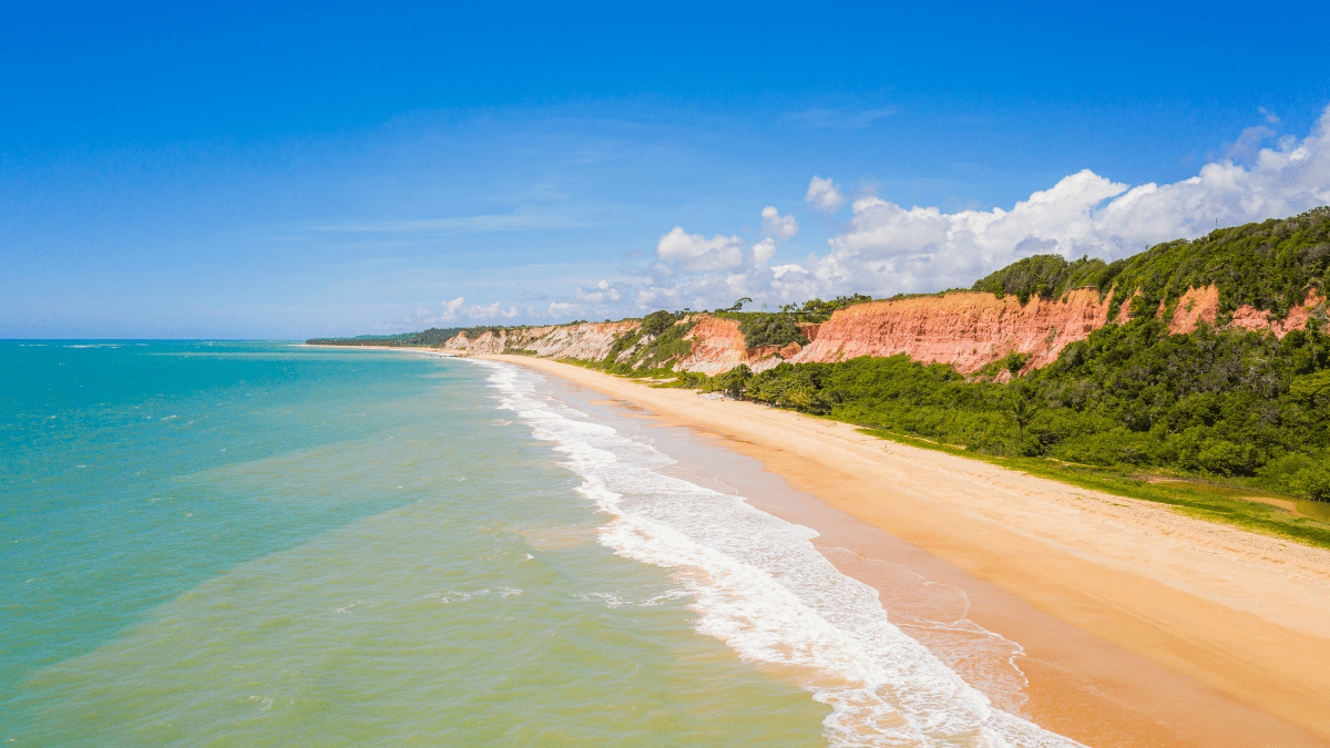 Vista aérea da praia em Porto Seguro com falésias, mar azul e faixa de areia clara