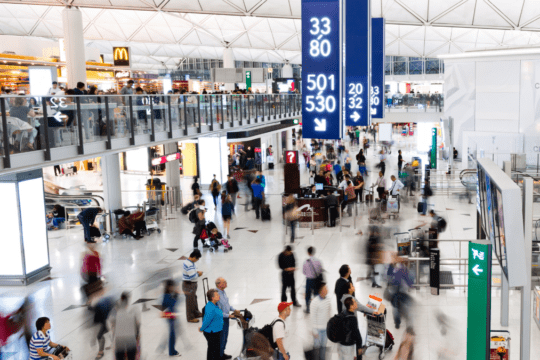 Área interna de aeroporto com grande circulação de passageiros e painéis de sinalização aérea