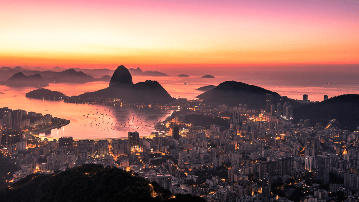 Vista aérea do Rio de Janeiro ao entardecer, com o Pão de Açúcar e a Baía de Guanabara