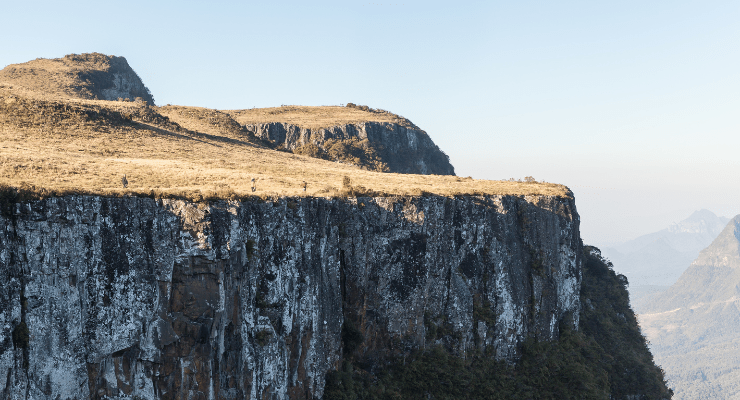 Paredão rochoso na Serra Catarinense em Urubici (SC), com vegetação de altitude e vista ampla das montanhas ao fundo.