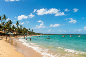 praia tropical no Nordeste com mar azul-turquesa, coqueiros, areia clara e barcos próximos à costa